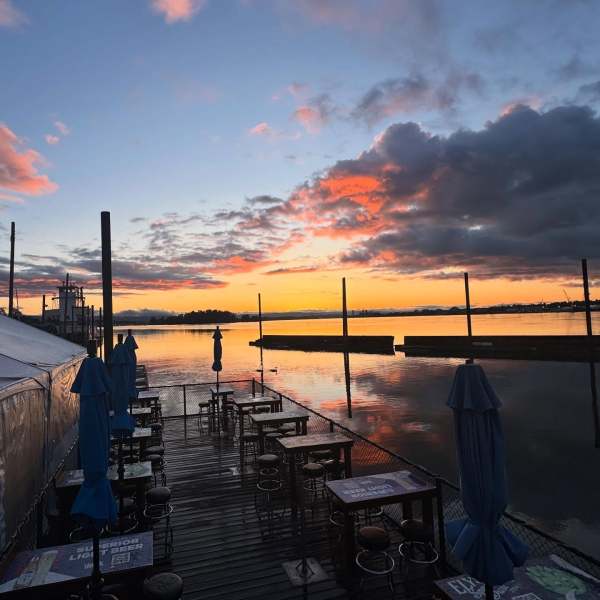 Sunset over a lakeside deck with tables and closed umbrellas.