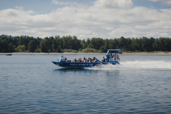 Blue speedboat labeled 'Willamette' on a lake with passengers on a sunny day.