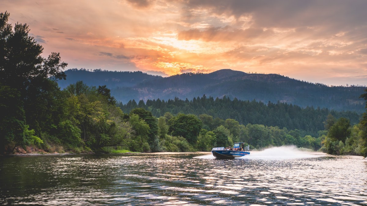 A speedboat on a river with trees and mountains at sunset.