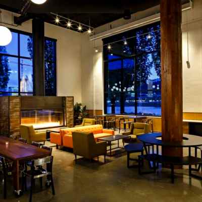 Modern lounge with tables, chairs, sofas, and a fireplace by large windows at night.